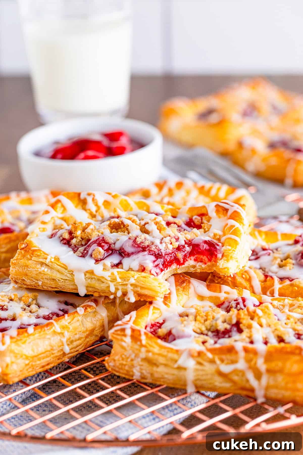 Cherry Danish with Cream Cheese: Flaky Pastry Recipe 7 Bite taken out of one cherry danish stacked on top of others on wire rack.