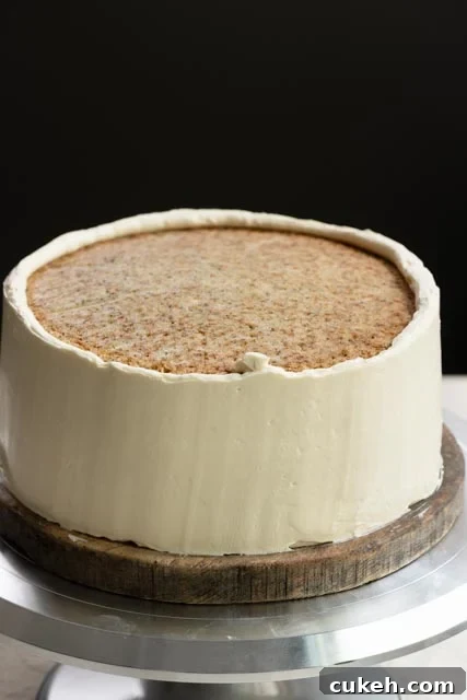 Partially frosted two layer cake with honey buttercream on a turntable.