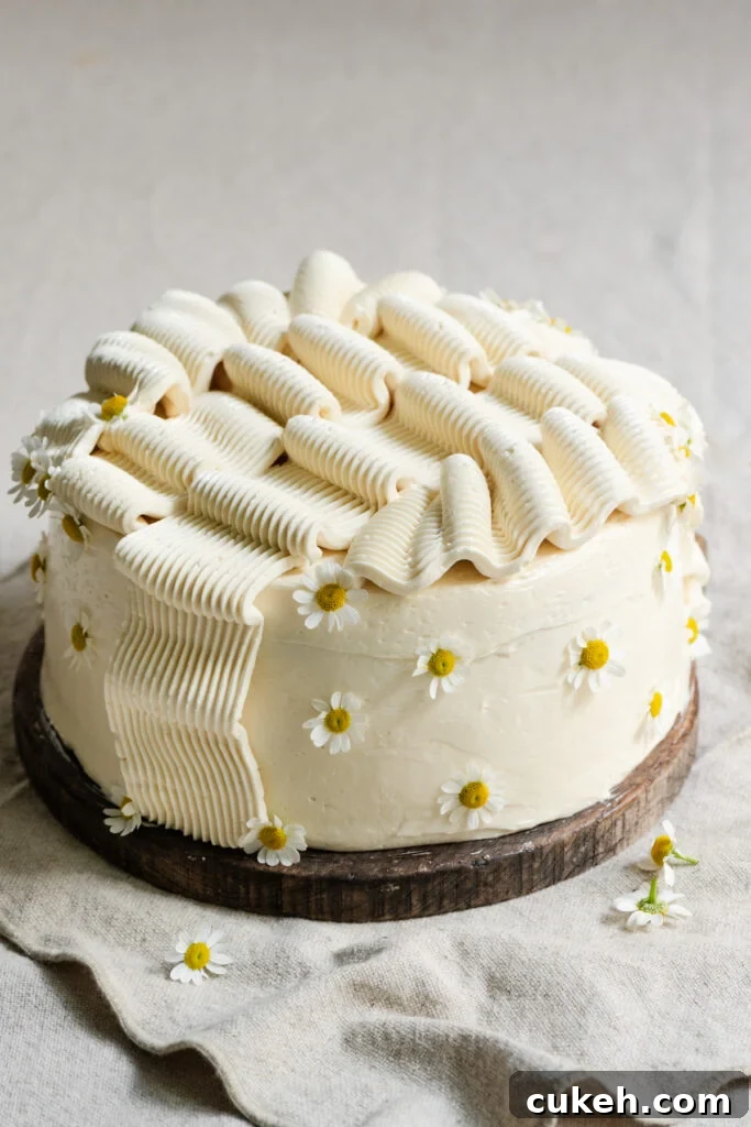Frosted banana layer cake, decorated with edible flowers on a wood cutting board.