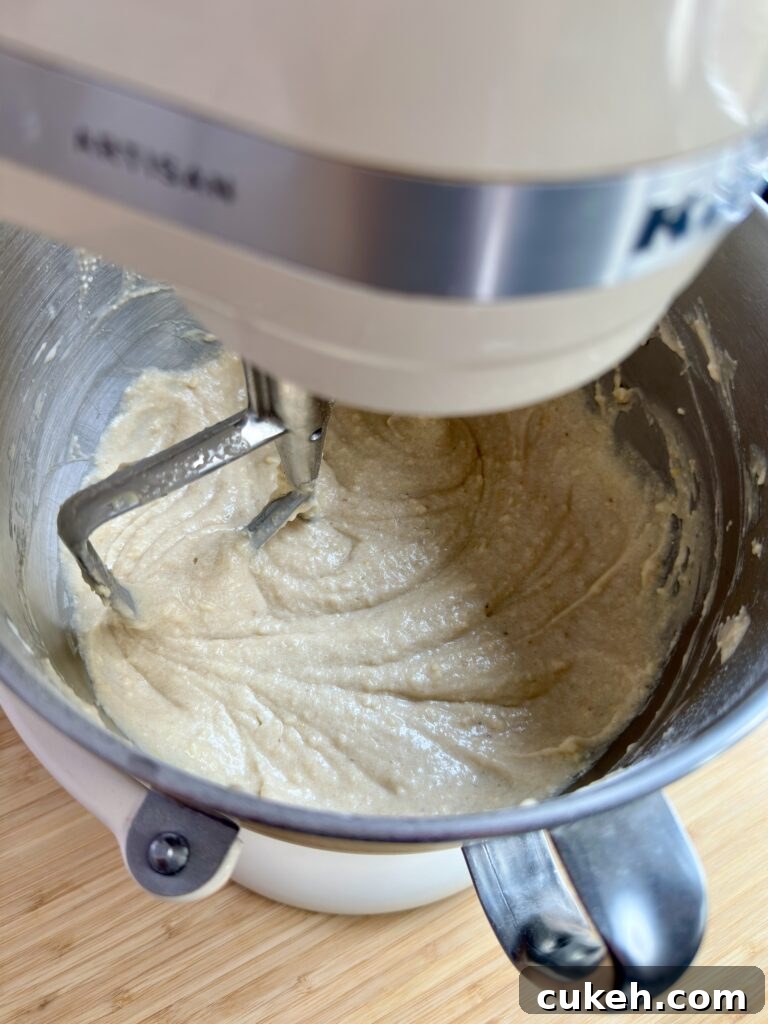 Banana cake batter being mixed in a stand mixer with paddle attachment.