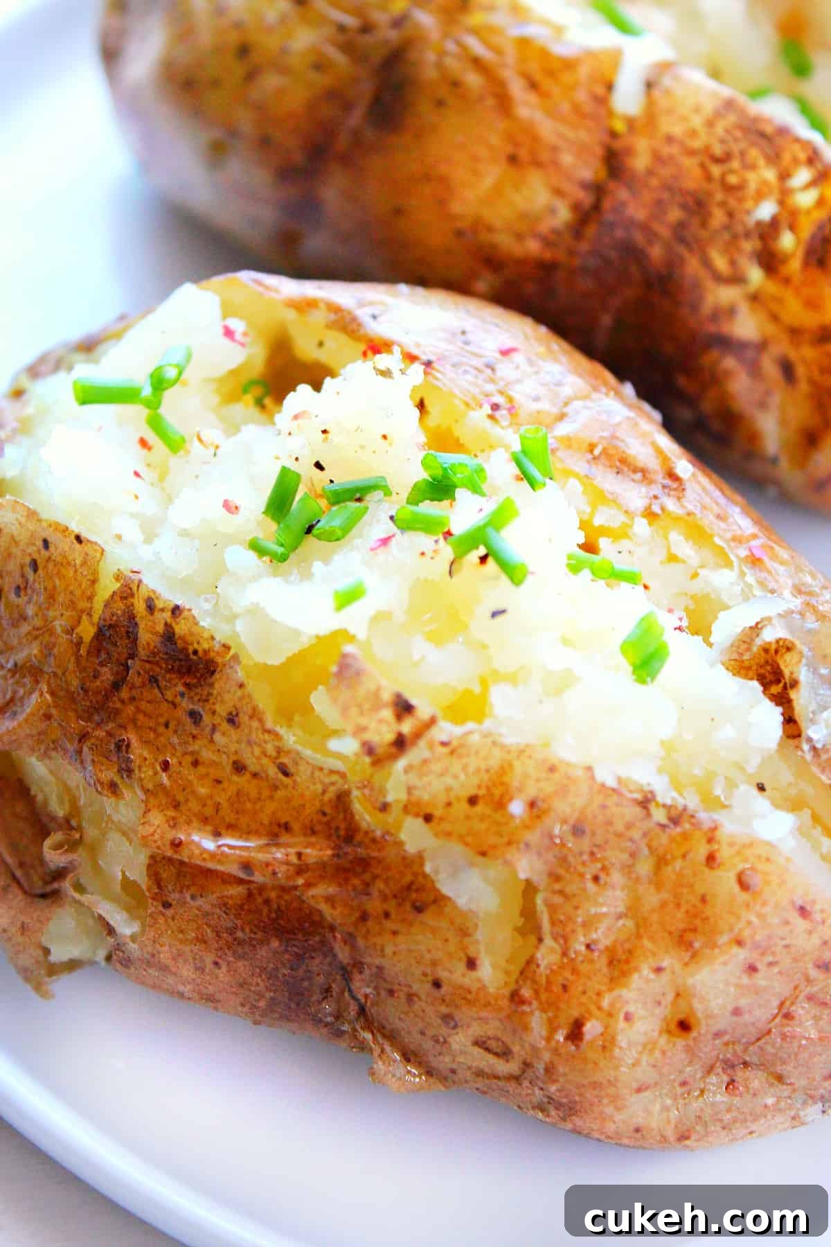 Microwave Baked Potatoes recipe Baked potato with butter and chives on a plate.