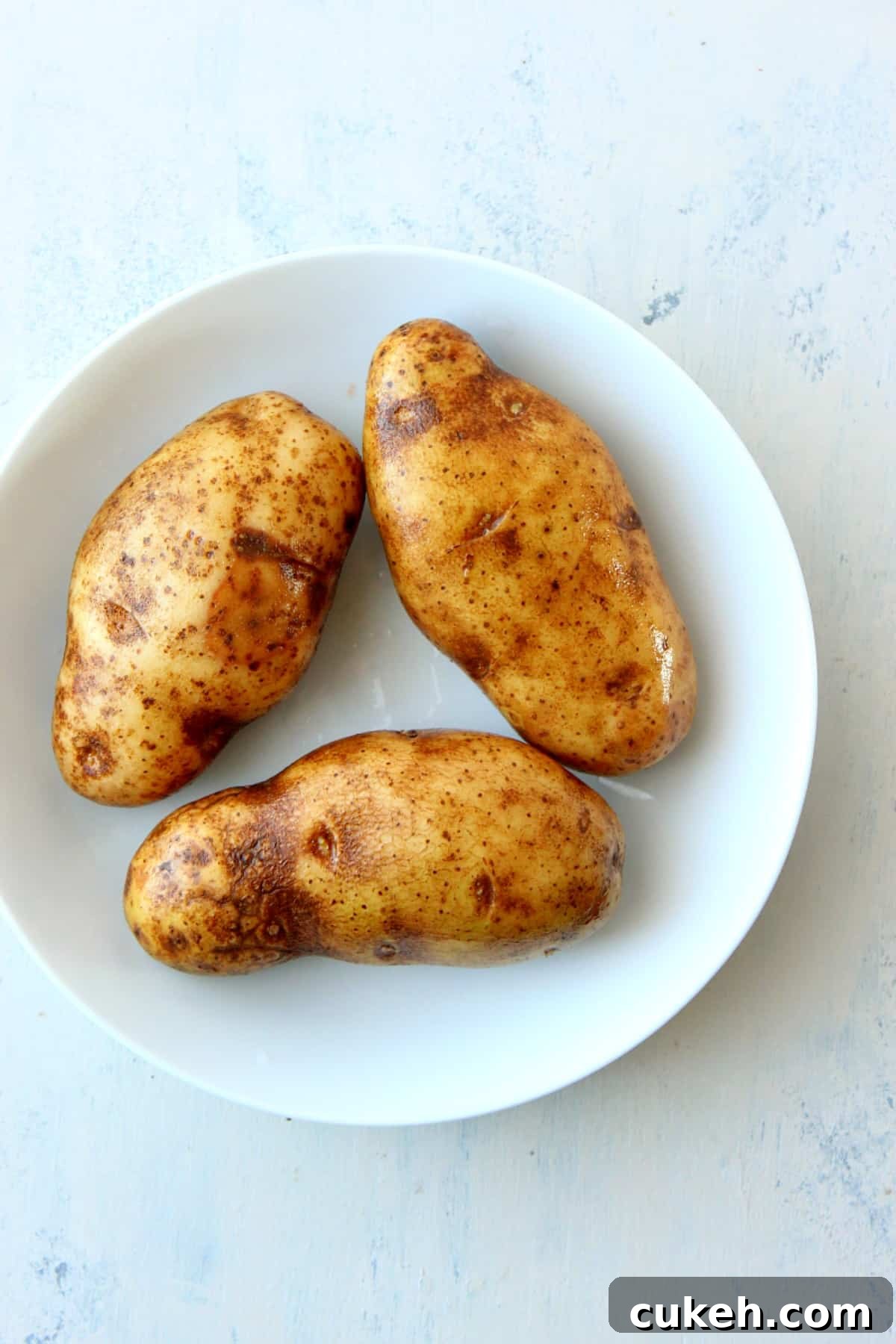 how to bake potatoes in the microwave Three potatoes in a white bowl.