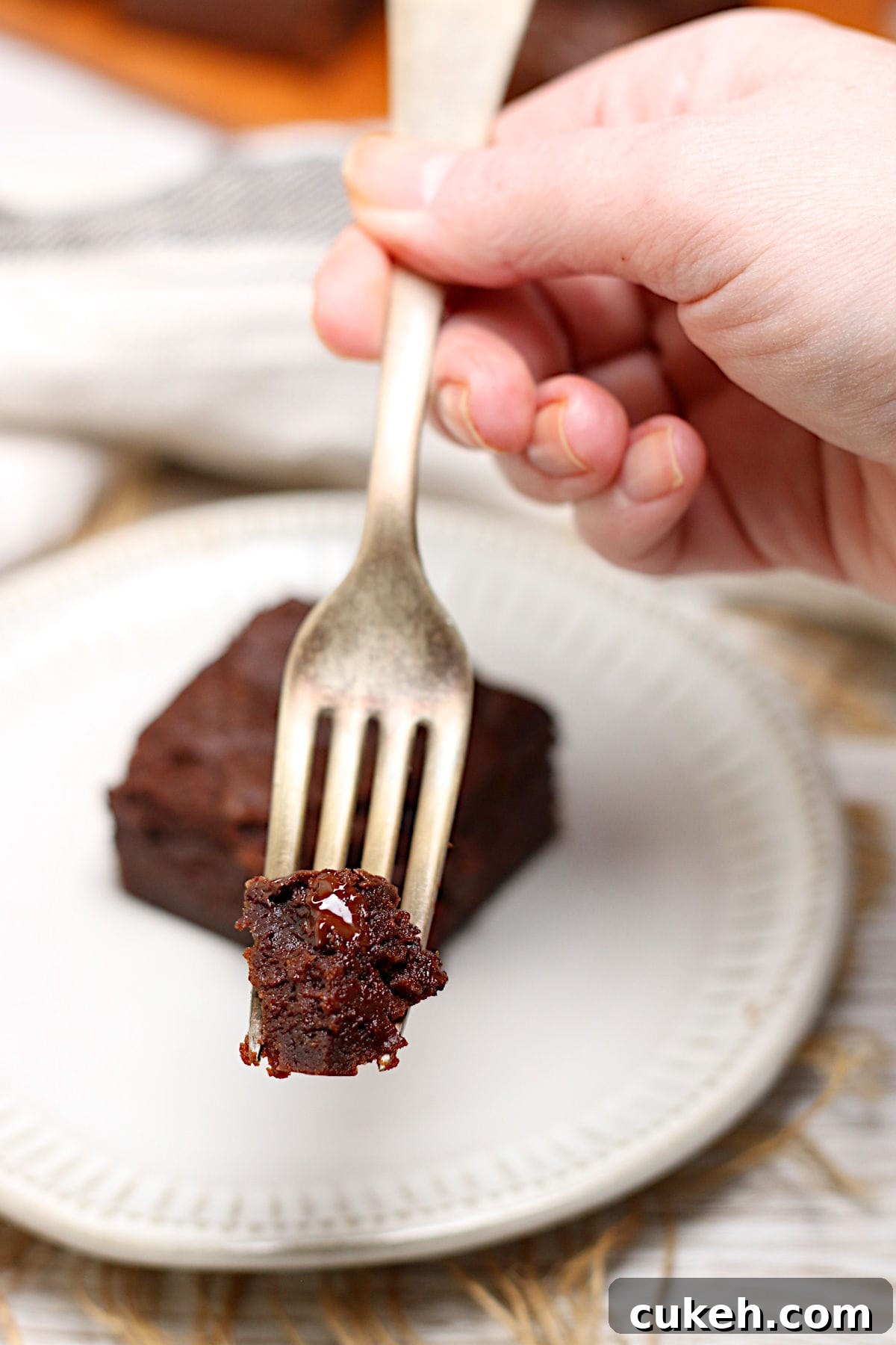 A hand holding a piece of Mocha Fudge Vegan Brownie on a fork.
