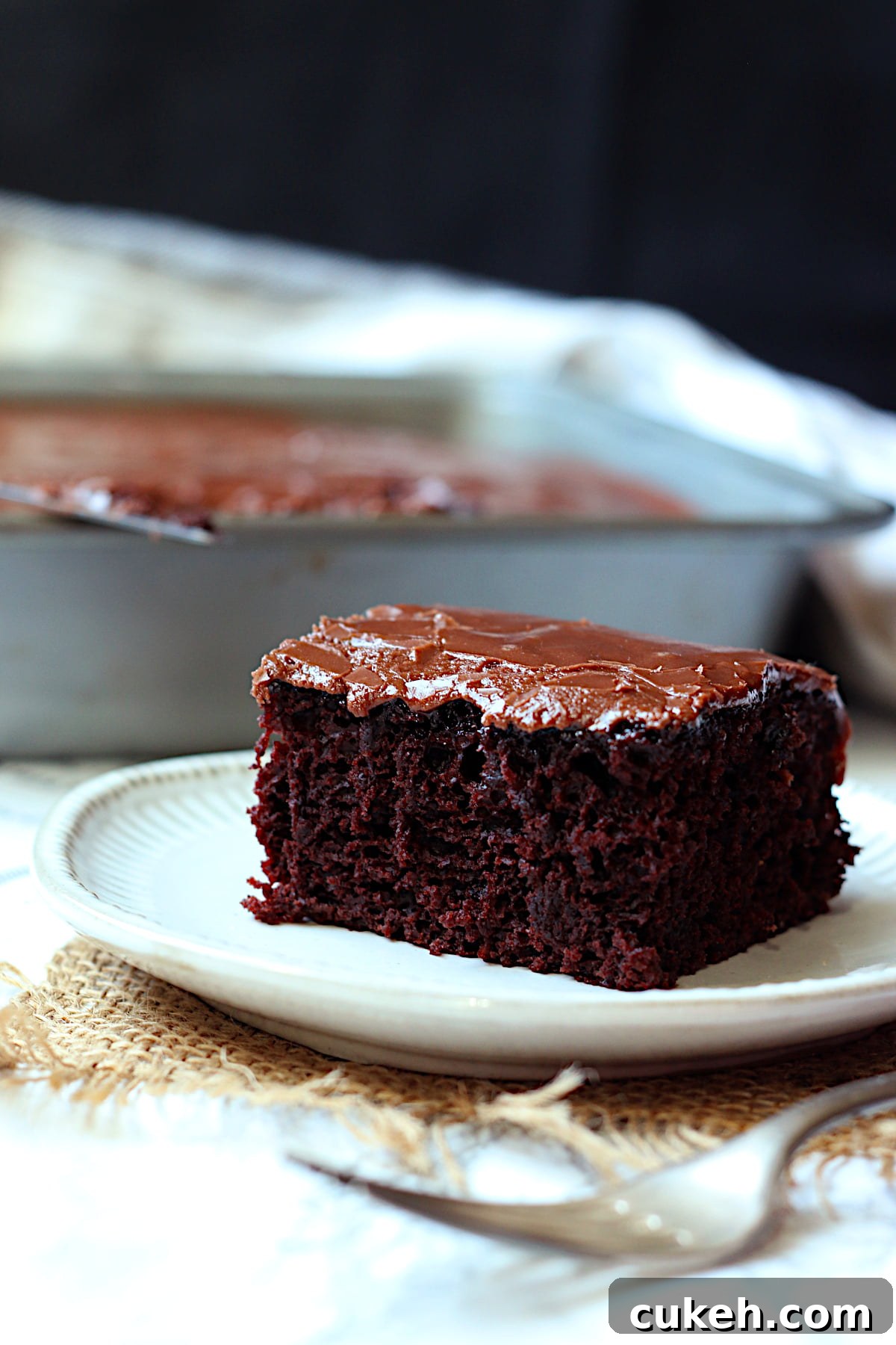 A slice of frosted Easy Chocolate Wacky Cake on a white plate.