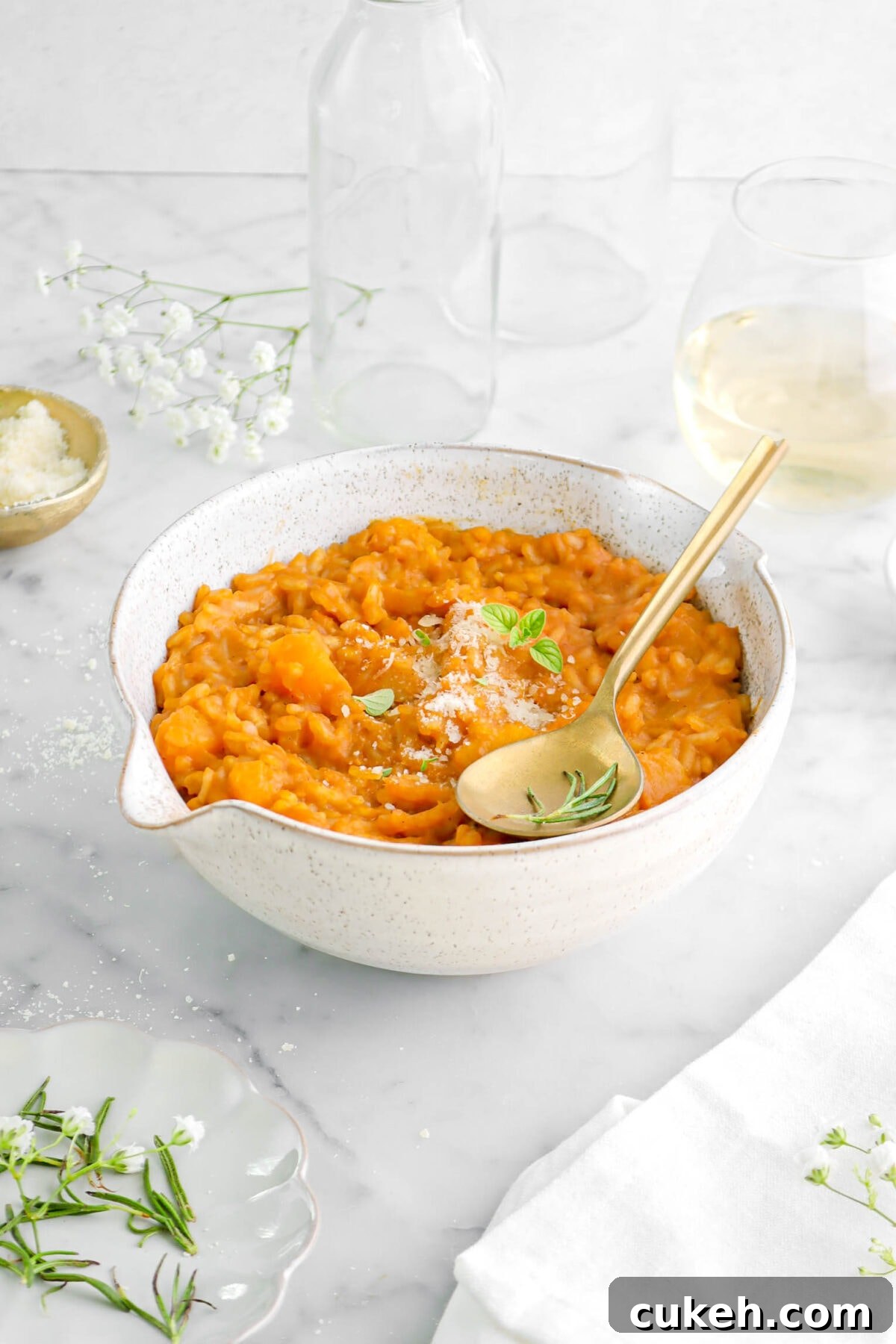 front shot of butternut squash risotto in large bowl with gold spoon on top, with glass of wine behind.