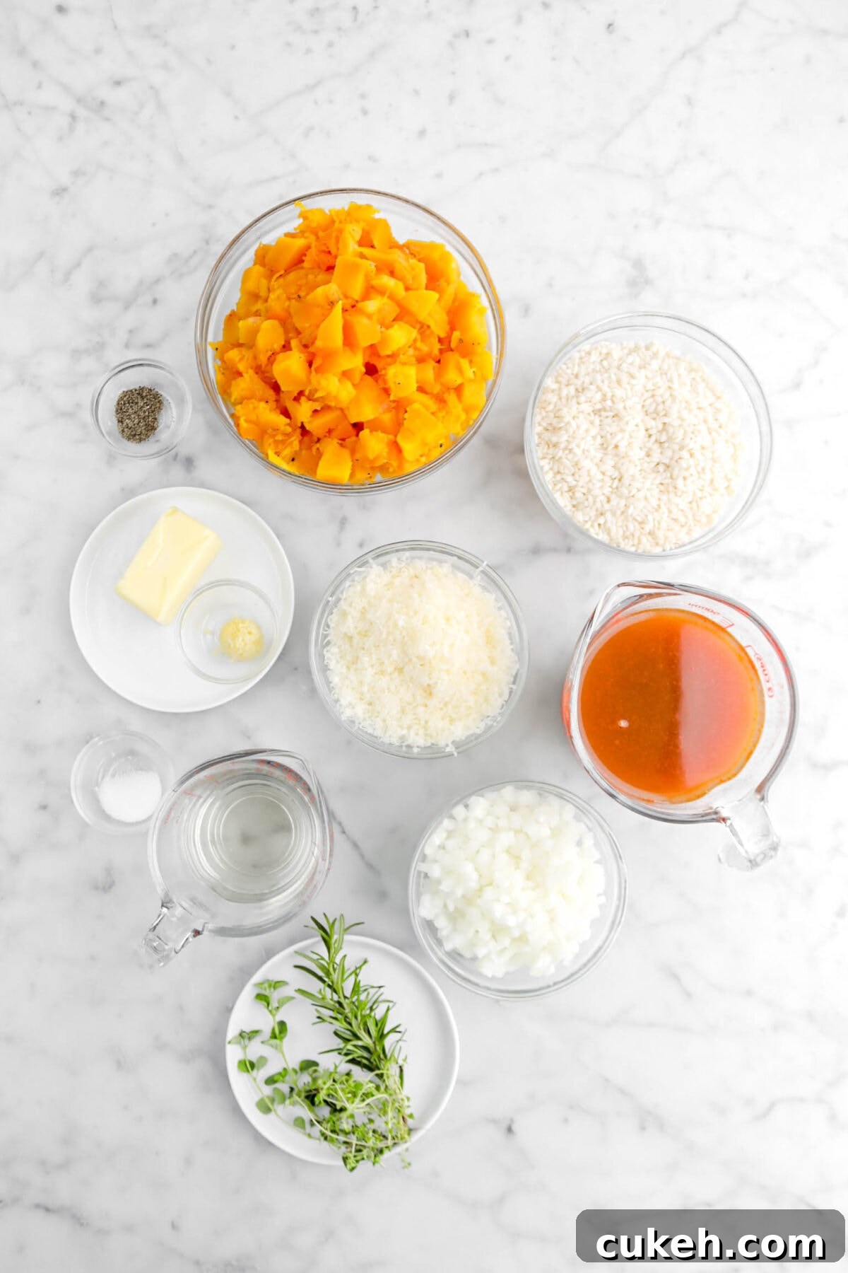 ground pepper, chopped butternut squash, arborio rice, butter, minced garlic, grated parmesan, broth, chopped onion, salt, white wine, and herbs on marble surface.