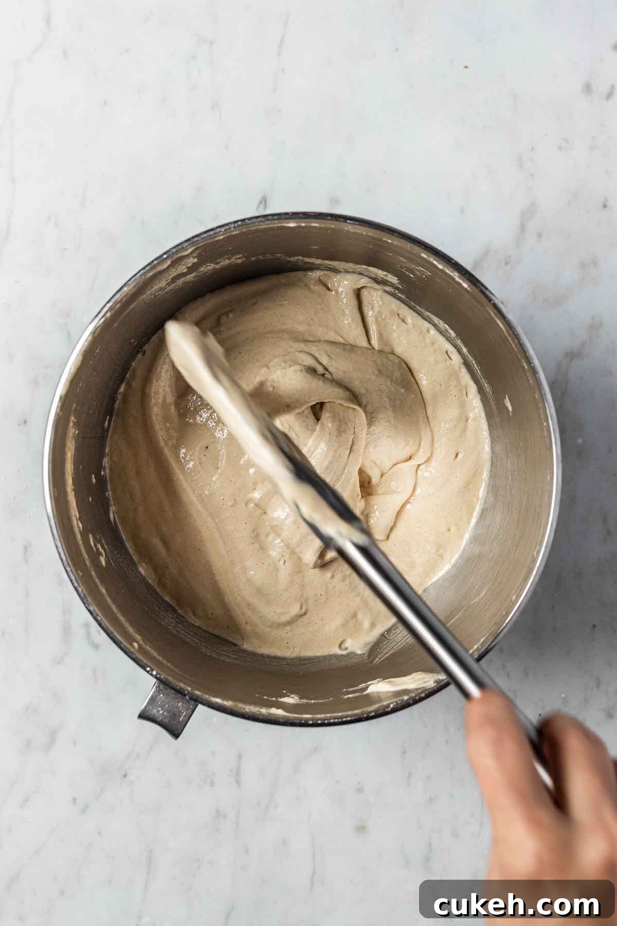 A spatula drizzling finished macaron batter back into the mixing bowl to demonstrate consistency.