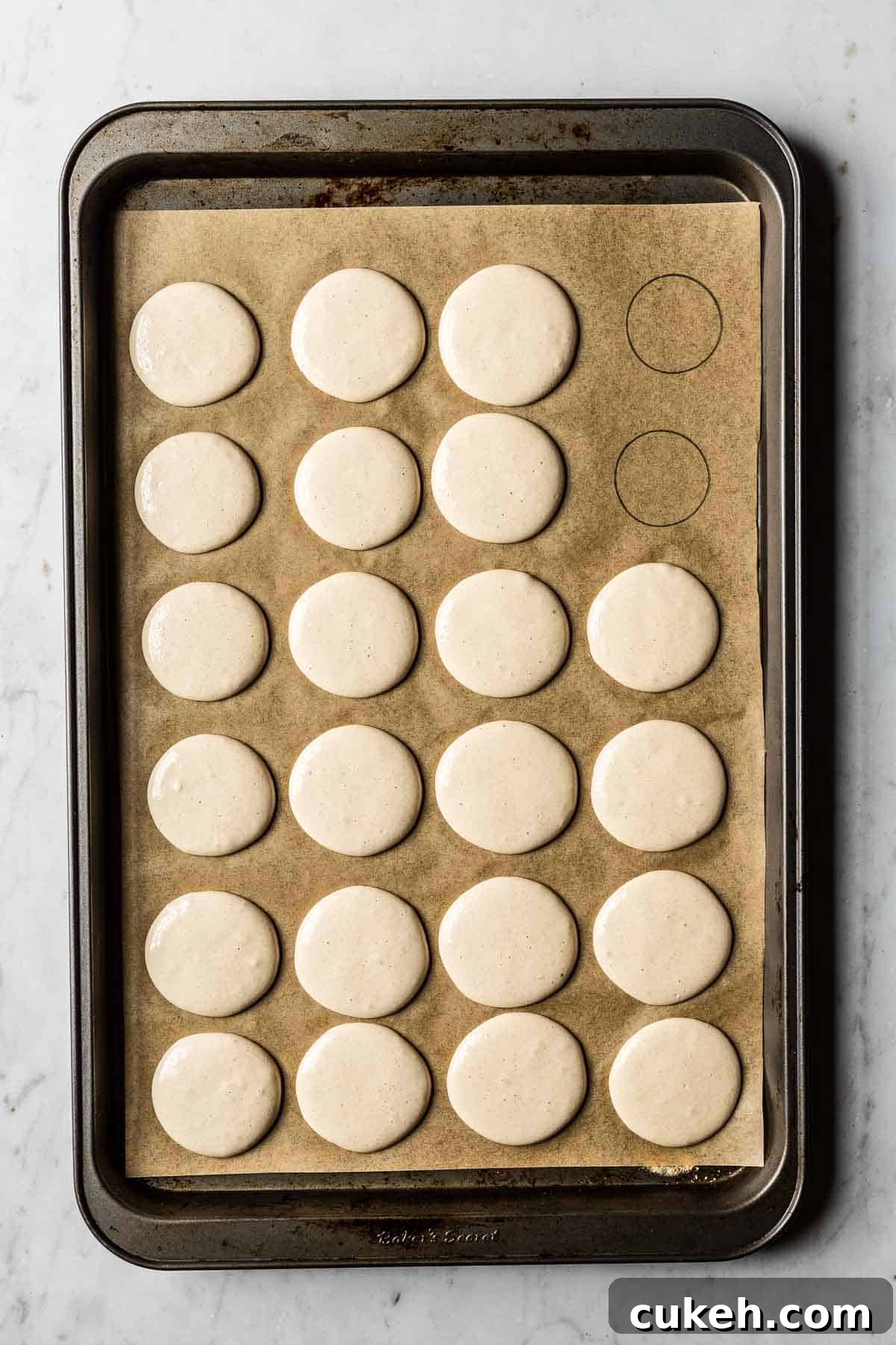 Piped macarons curing on a parchment lined baking sheet.