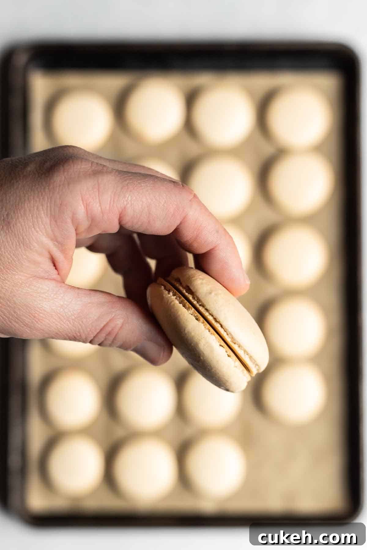 A white skinned hand holding two macaron shells together in a sandwich shape.