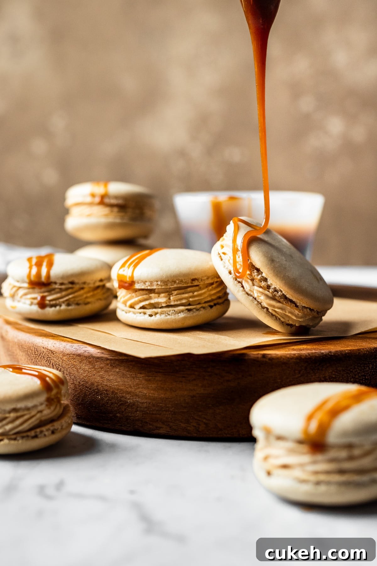Macarons on a wooden cutting board with a drizzle of caramel dripping onto a macaron.