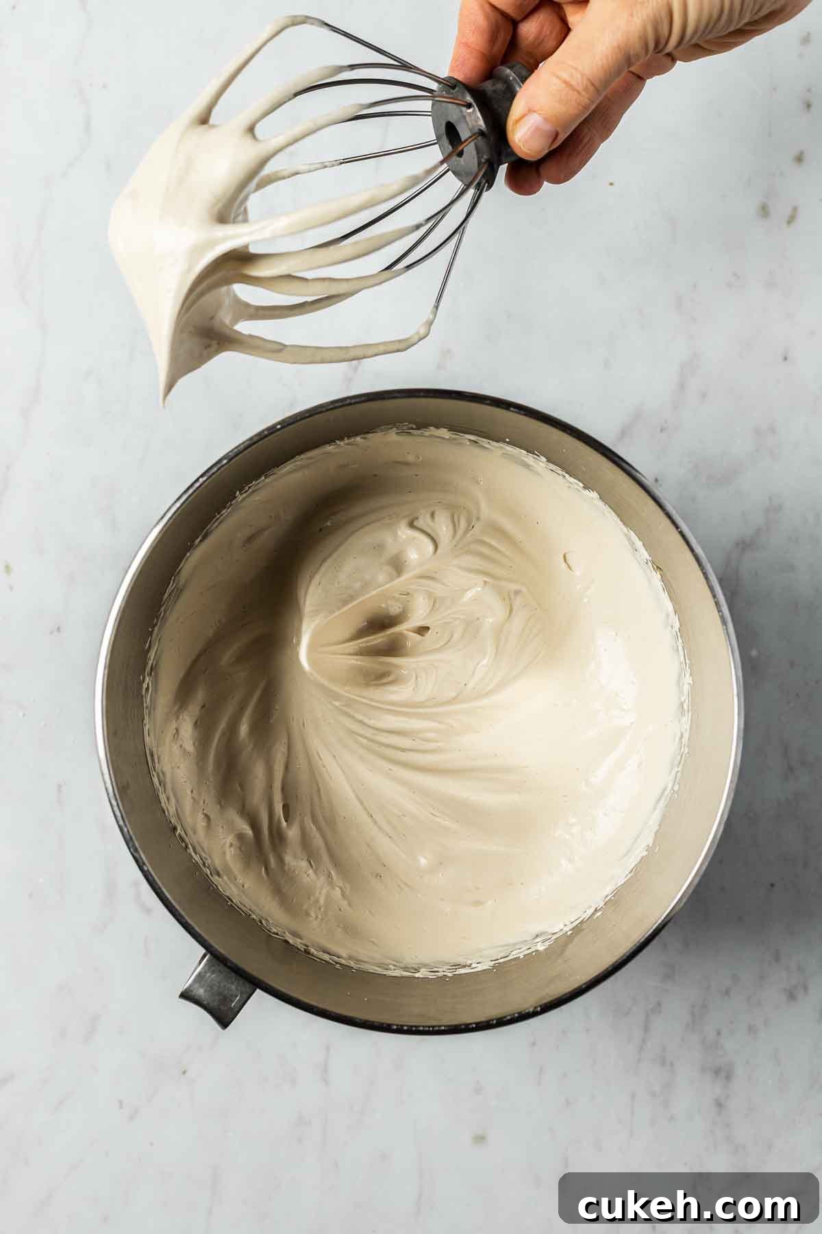 A mixing bowl of stiffly whipped meringue and a whisk showing stiff peaks.
