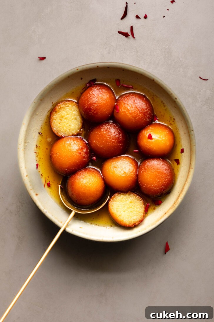 A bowl of Gulab Jamun with one cut in half showing the inside texture.