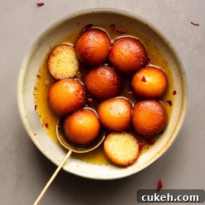 A bowl of Gulab Jamun with one cut in half showing the inside texture.