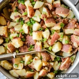 german potato salad with diced red potatoes, green onions, and bacon in a stainless steel skillet on a marble surface