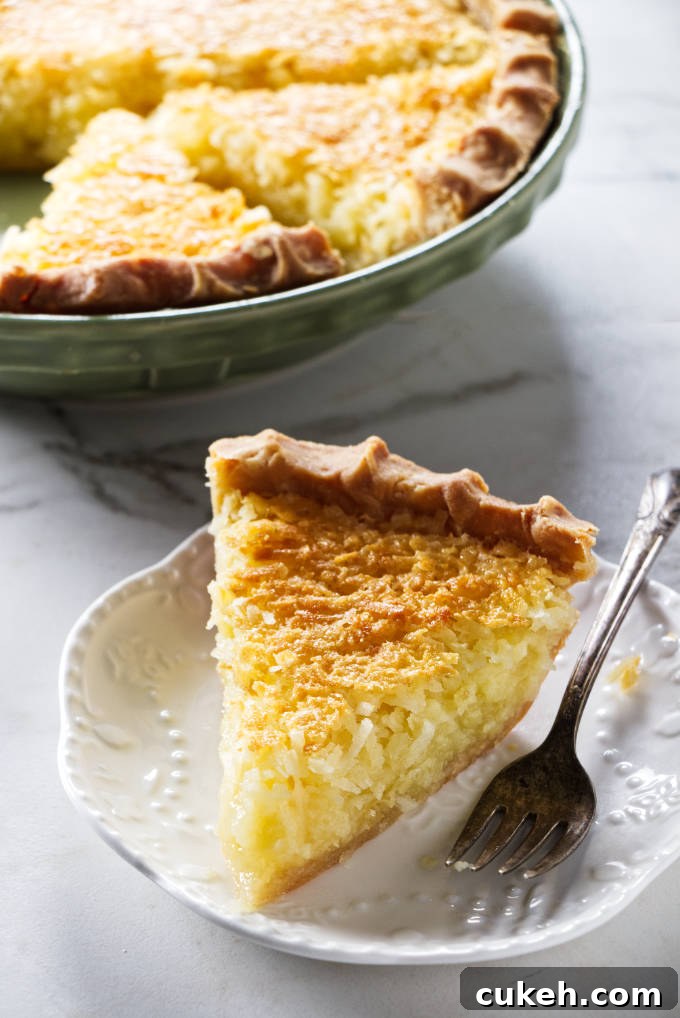A slice of coconut pie with a pie dish in the background.
