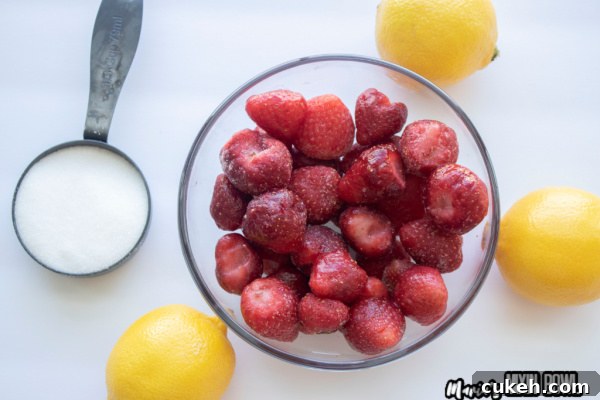 Overhead shot of strawberries in bowl, whole lemons, and measuring cup with sugar