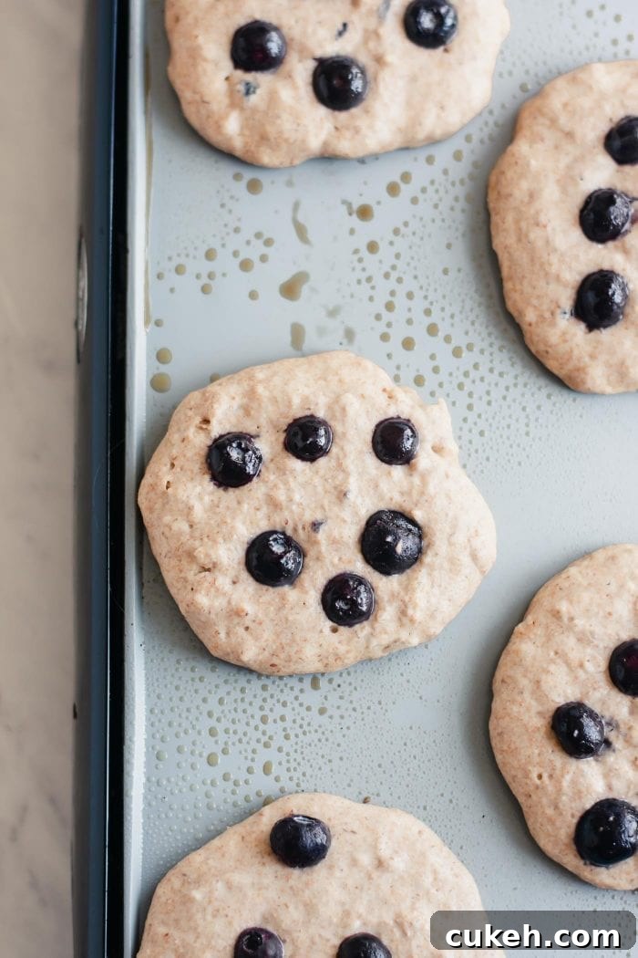 Vegan coconut pancakes with blueberries cooking on a pancake griddle.
