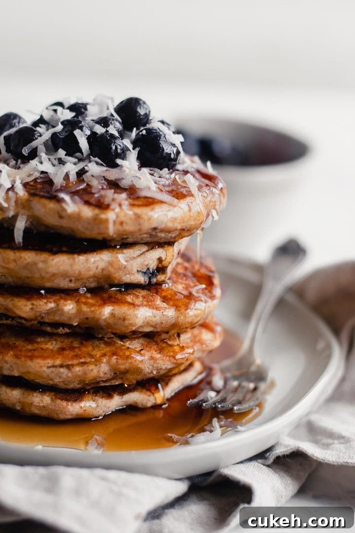 Close up shot of vegan blueberry pancake with maple syrup dripping down the pile.