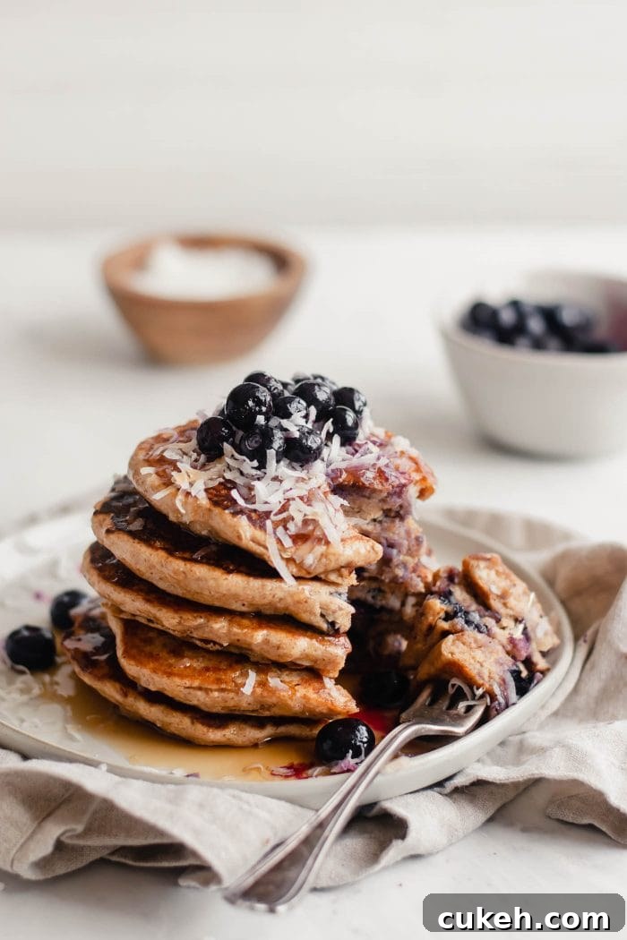 Stack of vegan blueberry coconut pancakes topped with blueberries and coconut.