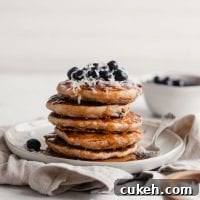 Stack of vegan blueberry coconut pancake with blueberries and coconut on top.