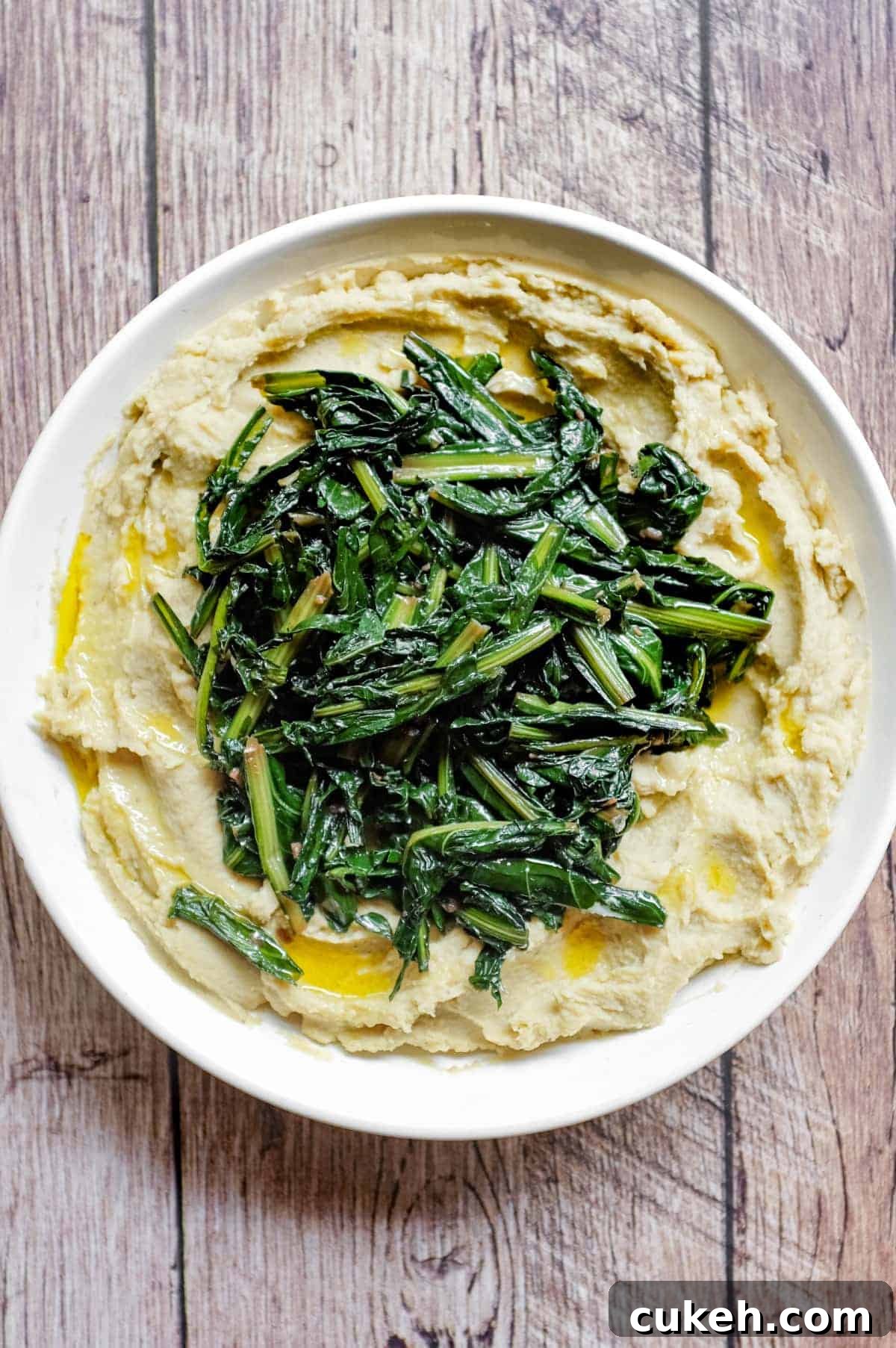 An overhead photograph of a large platter of fava bean puree topped with dark green chicory leaves