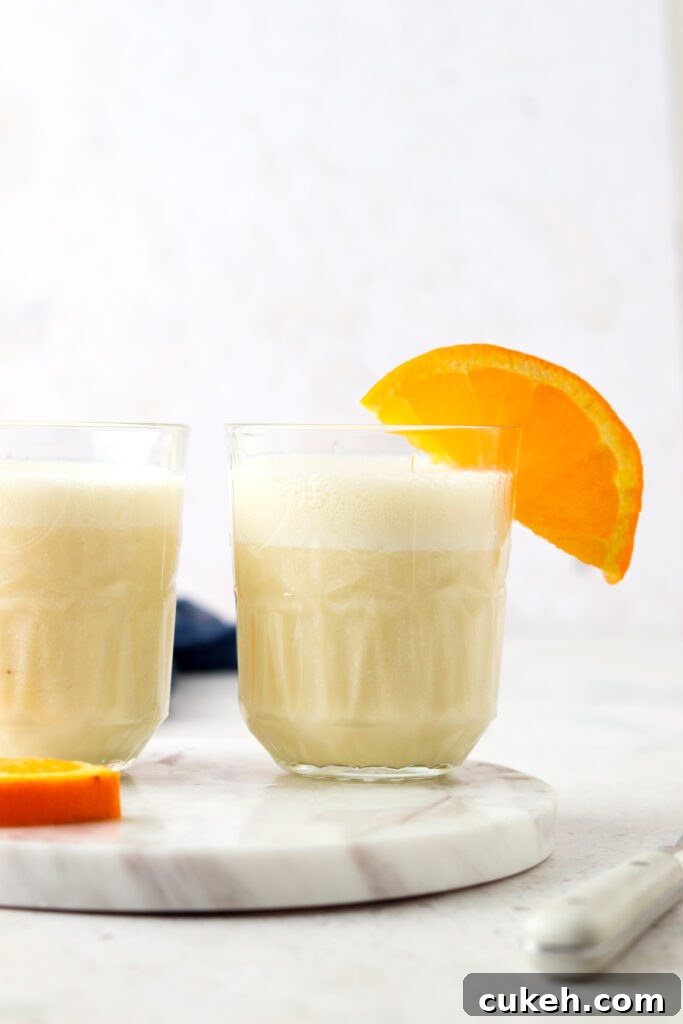 two orange creamsicle smoothies in a glass with oranges on top and a blue napkin