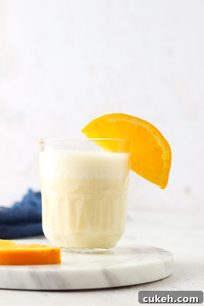 orange creamsicle smoothie in a glass with an orange on it and blue napkin