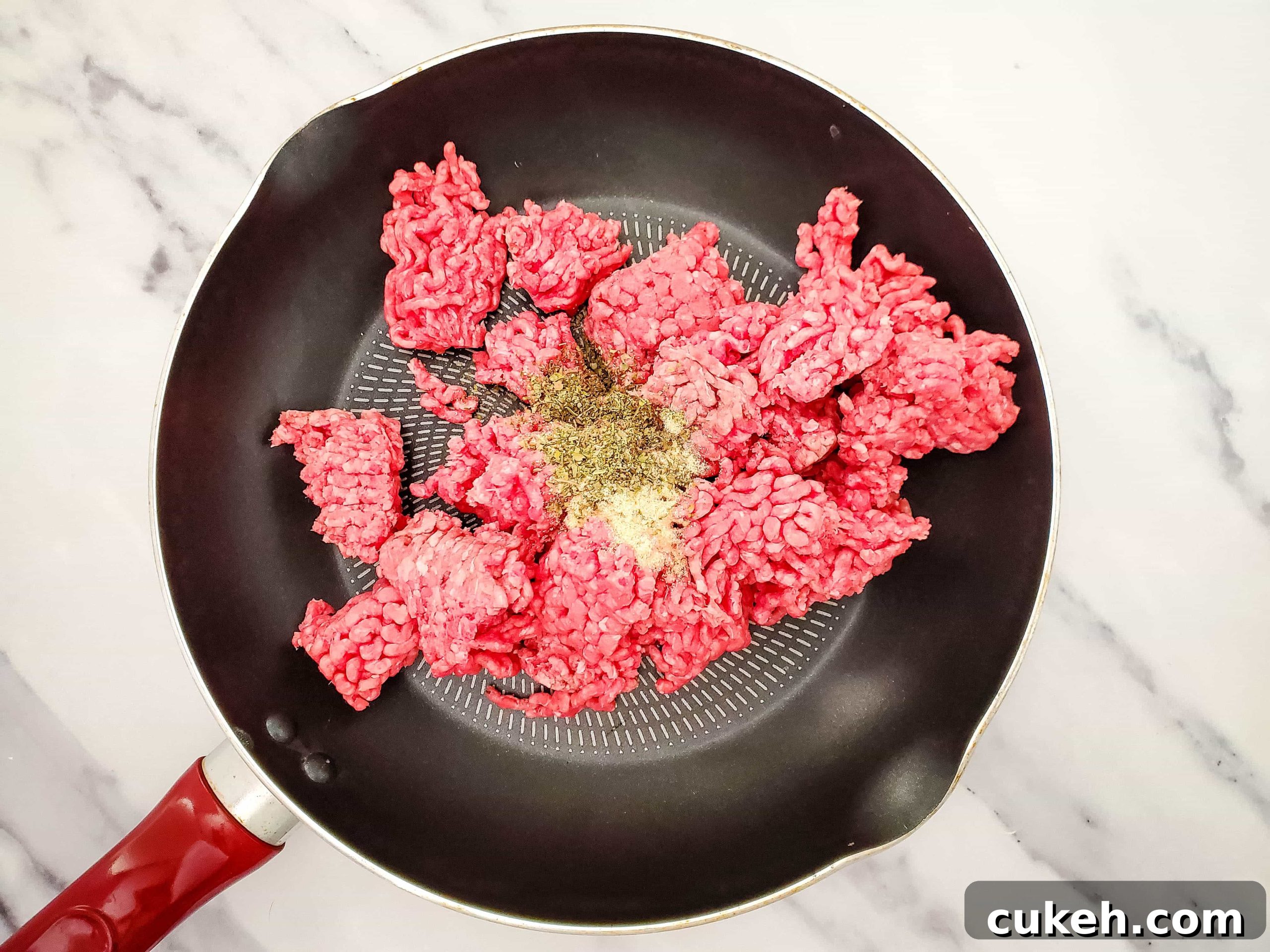 Photo of cooking skillet with raw ground beef and spices.