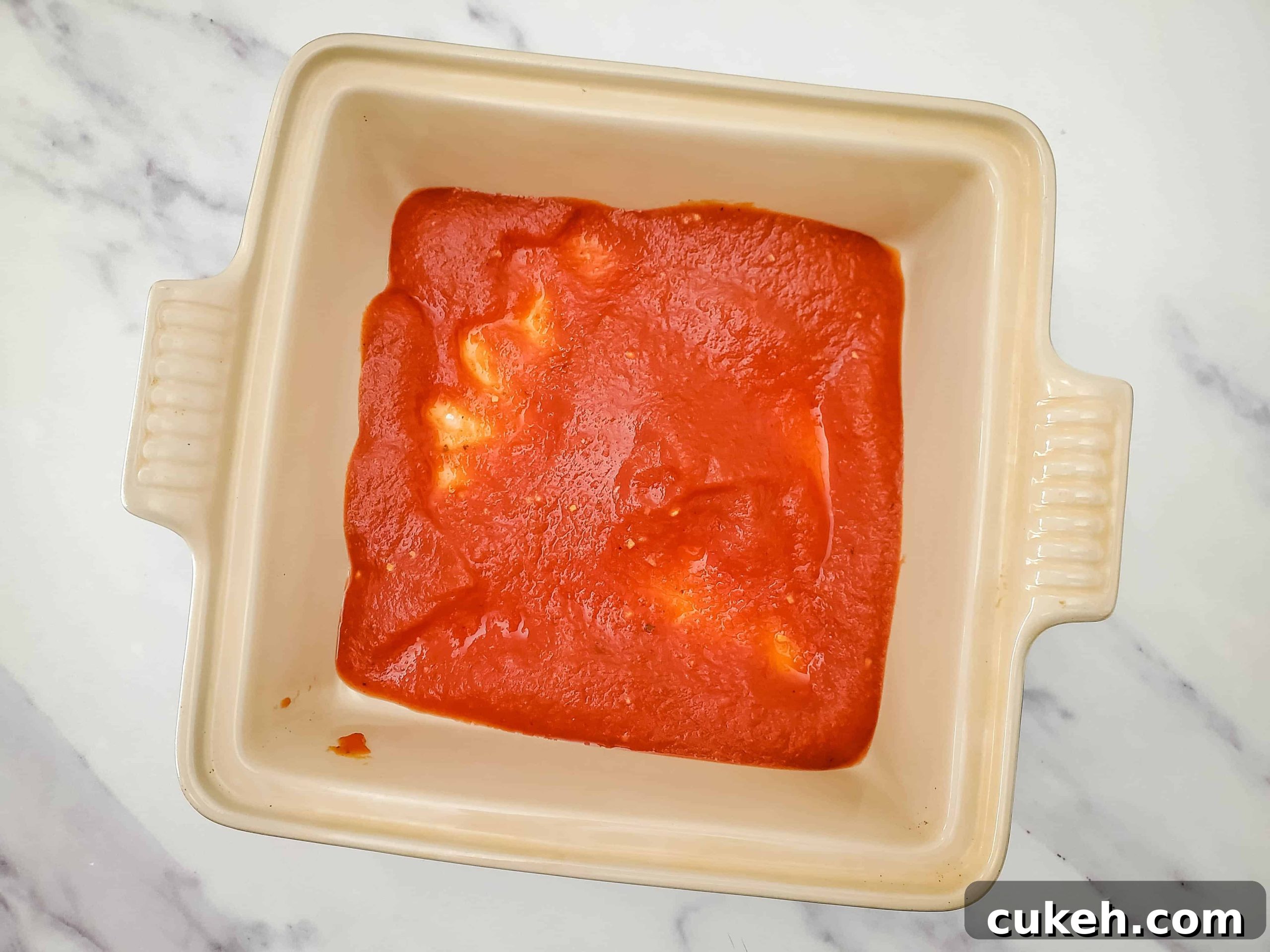 Glass baking dish with layer of pasta sauce evenly distributed