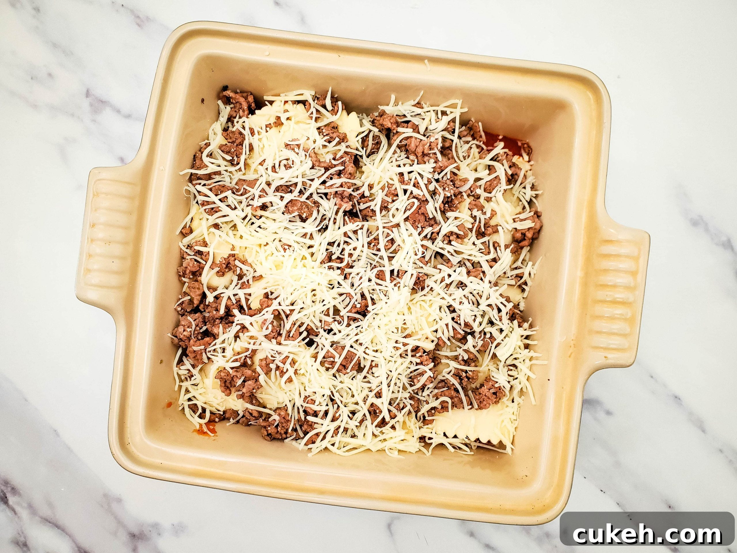 Casserole baking dish with layered pasta sauce, frozen ravioli, ground beef, and mozzarella cheese