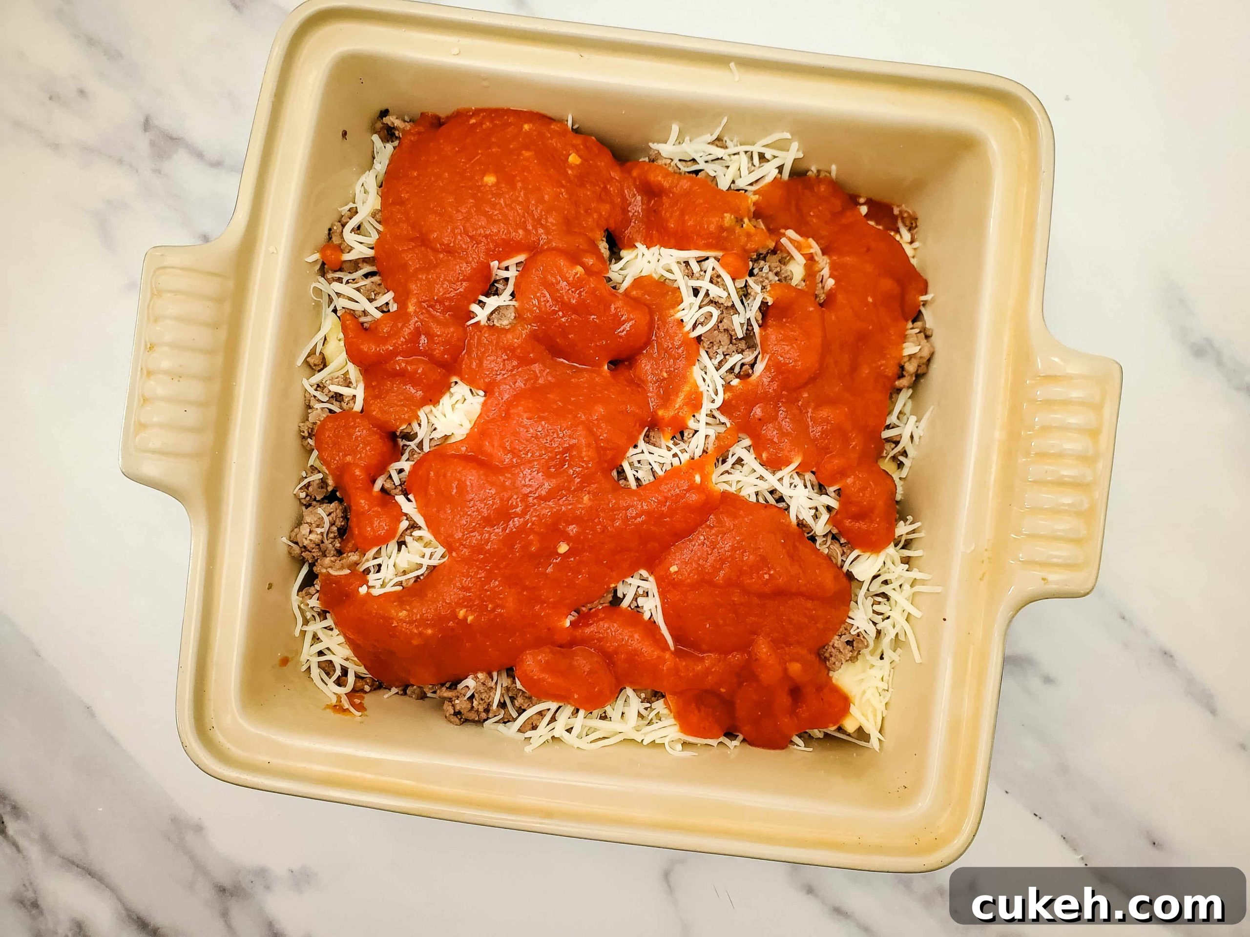 Casserole baking dish with layered frozen ravioli recipe and pasta sauce on top of a marble counter