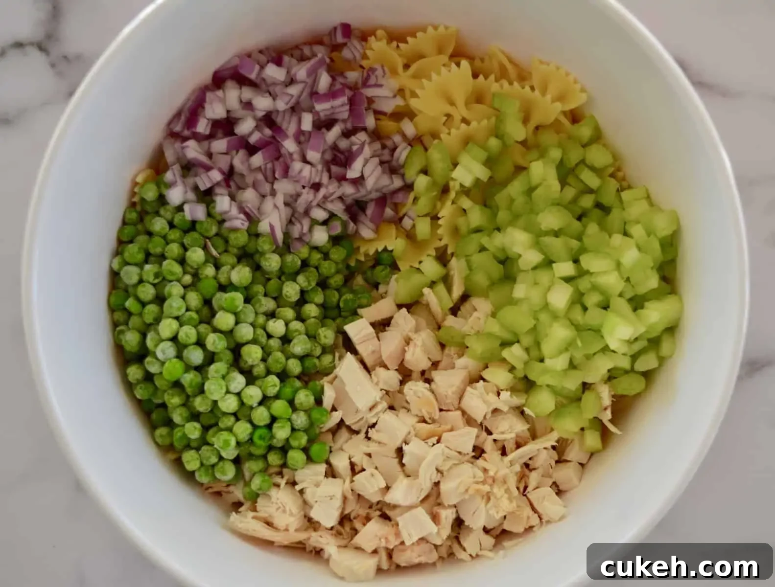 white bowl with pasta, celery, peas, and red onions. 