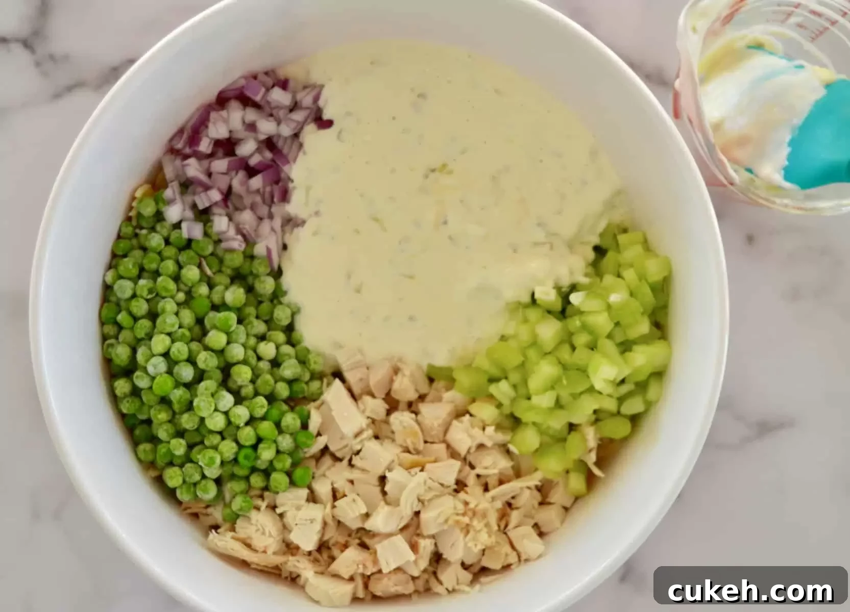 greek yogurt dressing in a white bowl along with pasta, peas, and red onion. 