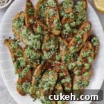 Air fryer fingerling potatoes on plate with green tahini sauce and serving spoon.. Lemons, extra tahini sauce, sesame seeds on the side.