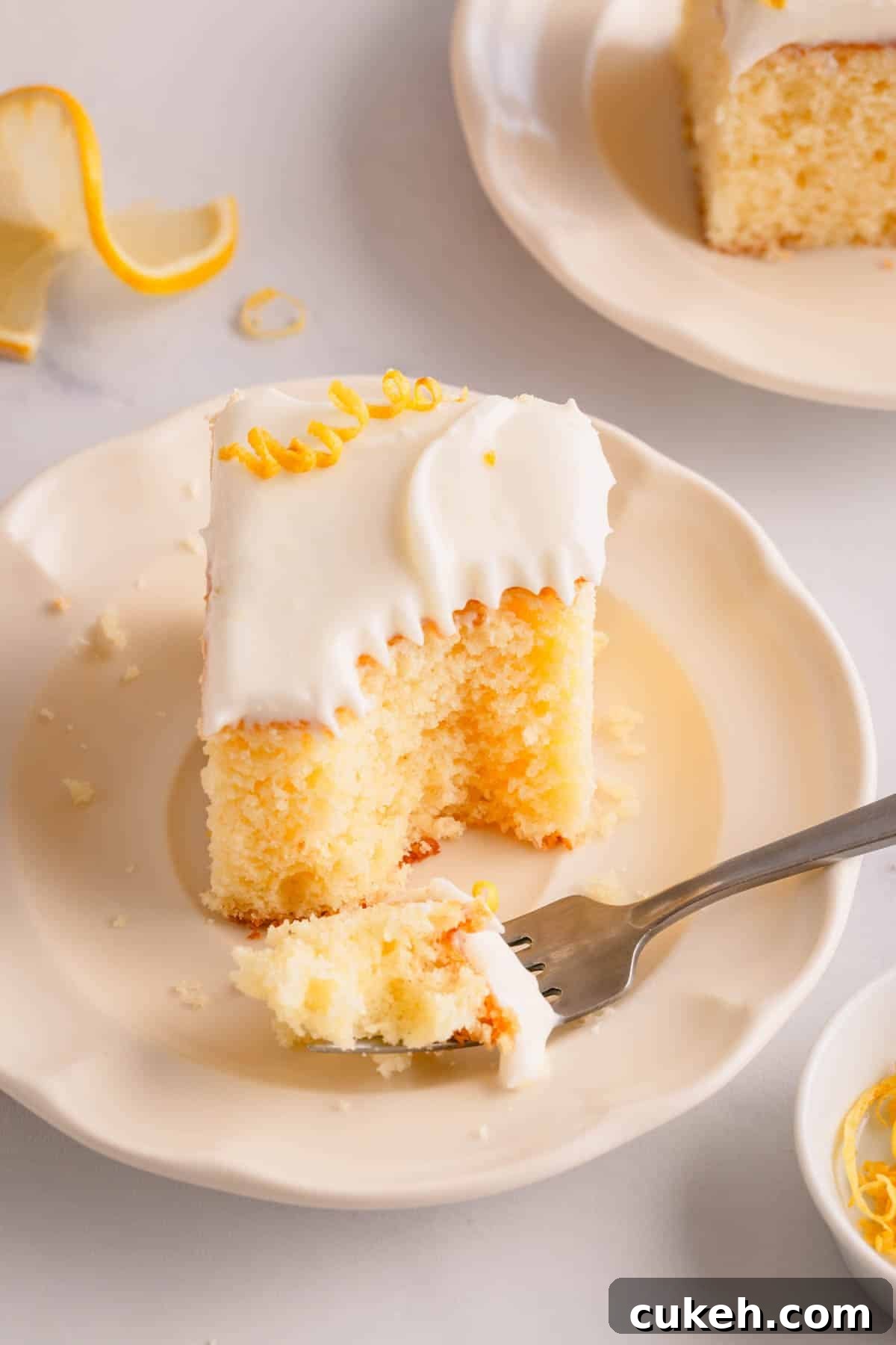 A slice of frosted lemon sheet cake on a plate with a fork holding a bite.