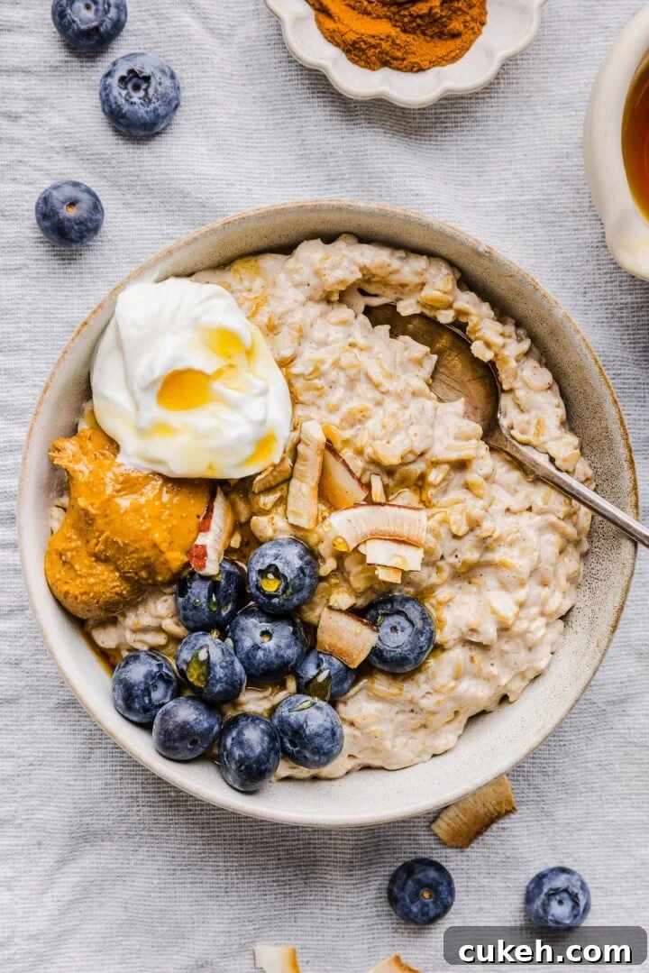 White bowl with greek yogurt oatmeal, topped with blueberries, nut butter, and extra yogurt.