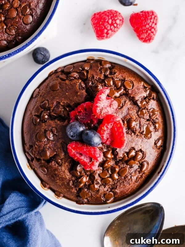 Birdseye photo of a ramekin filled with chocolate baked oatmeal, topped with raspberries and blueberries