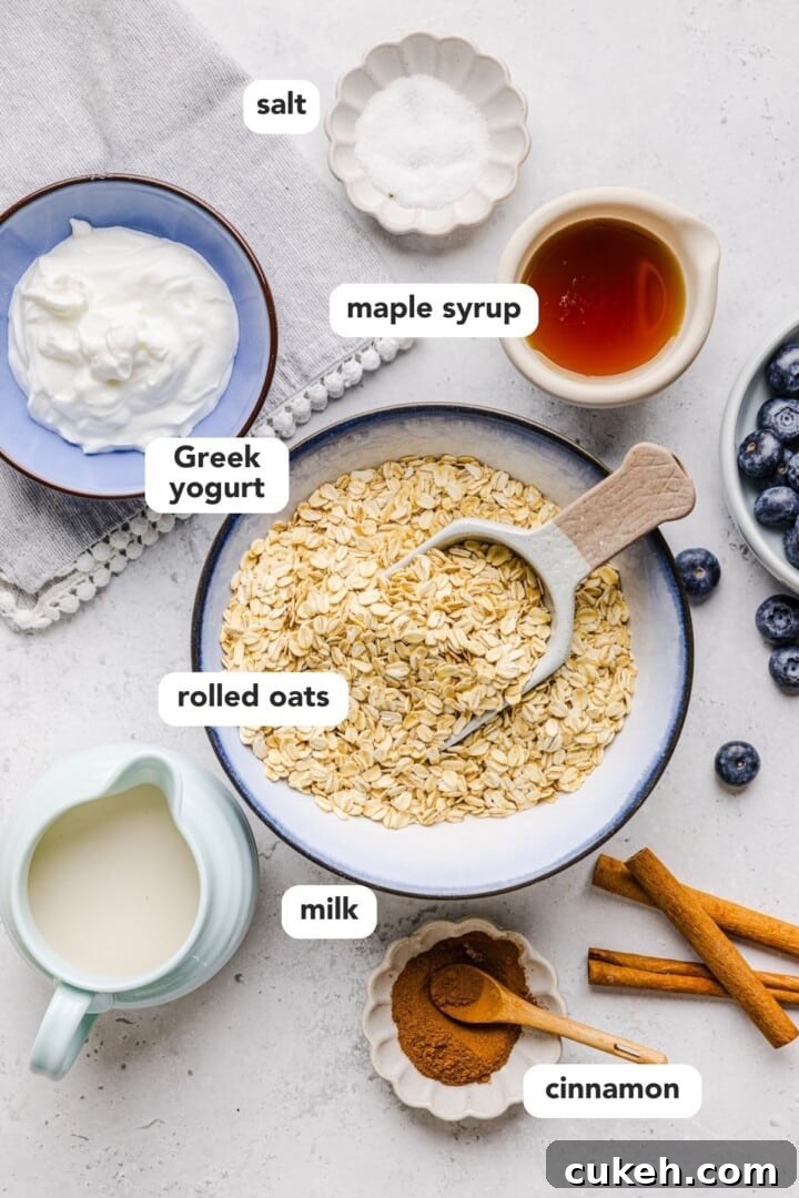 Ingredients for greek yogurt oatmeal displayed in small bowls on a white marble counter.