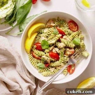bowl of pesto pasta with tuna and tomatoes with lemon on the side.