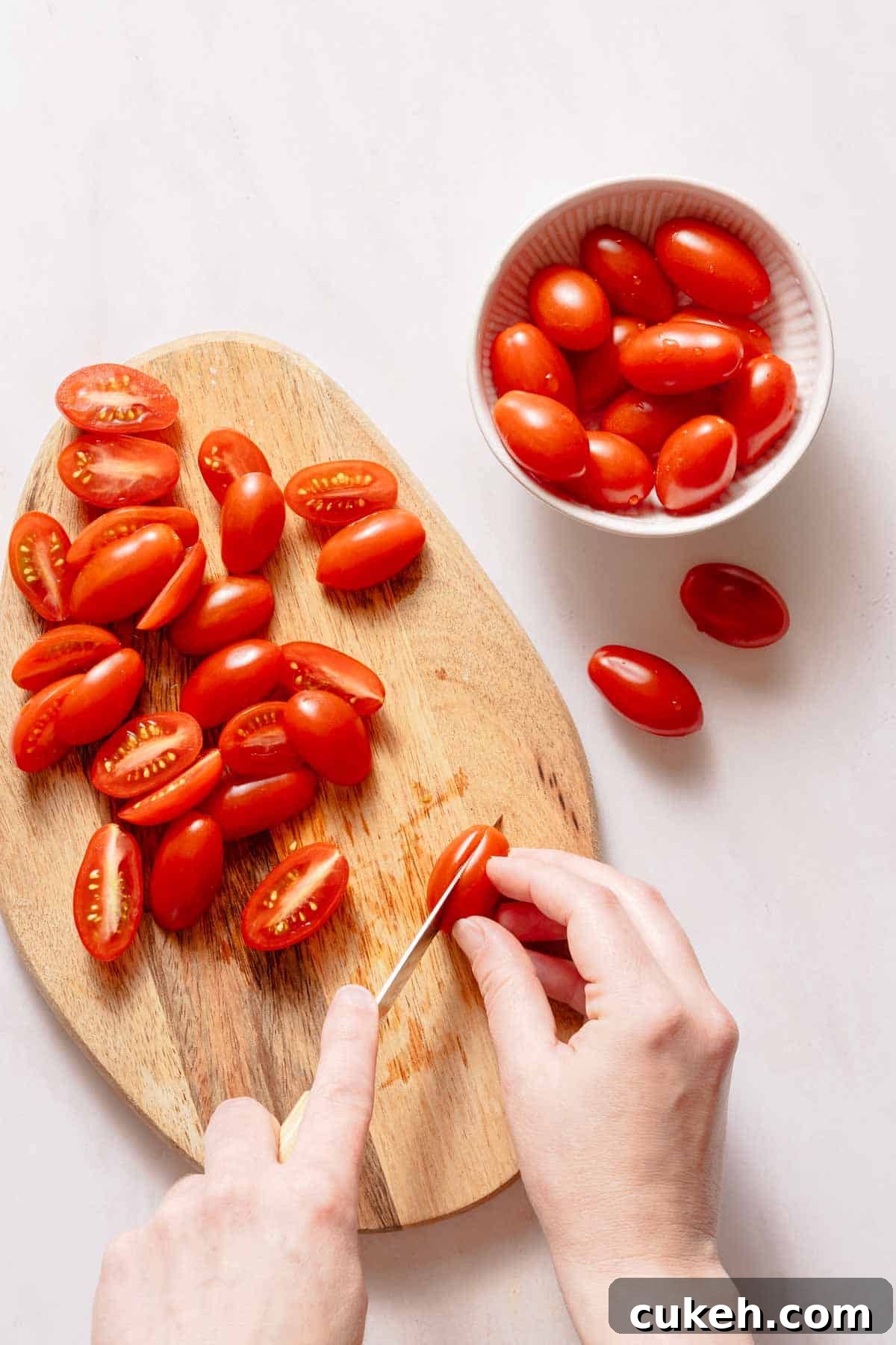 Creamy Tuna Pesto Pasta Recipe for Weeknight Dinners 4 cutting grape tomatoes in half on wooden cutting board.
