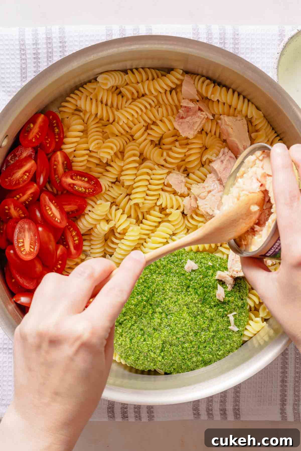 Creamy Tuna Pesto Pasta Recipe for Weeknight Dinners 5 tuna being added to pot with pasta tomatoes and pesto inside.