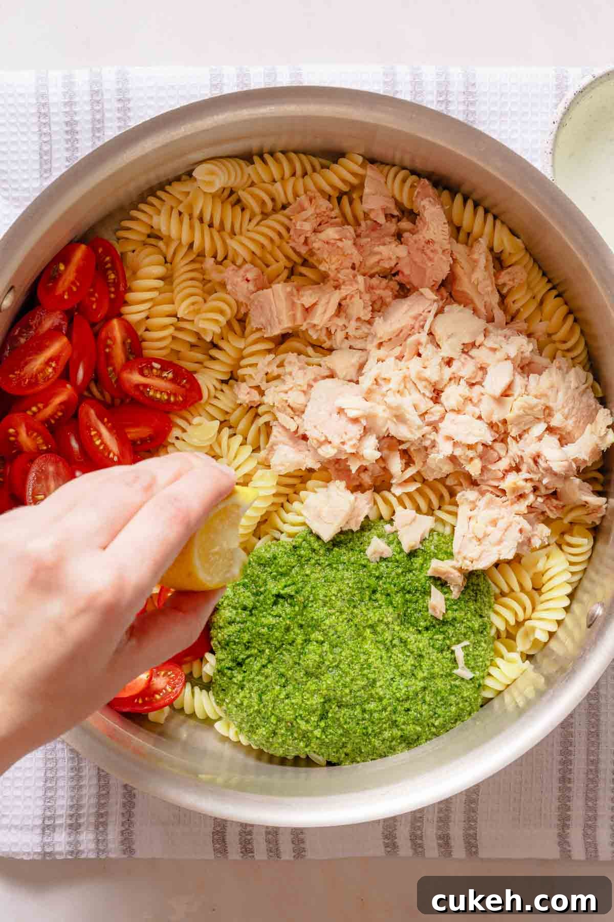 Creamy Tuna Pesto Pasta Recipe for Weeknight Dinners 6 wedge of lemon being squeezed into pot with tuna pesto pasta ingredients inside.