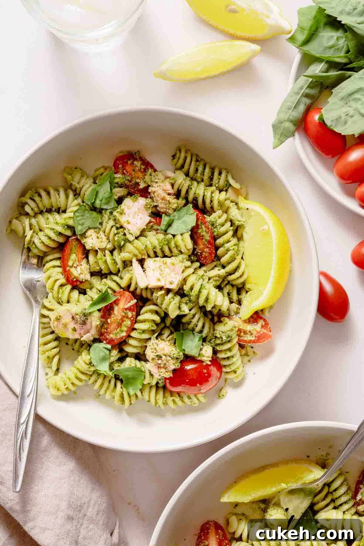 Creamy Tuna Pesto Pasta Recipe for Weeknight Dinners 7 two bowls of pasta with tomato tuna and lemon wedges.