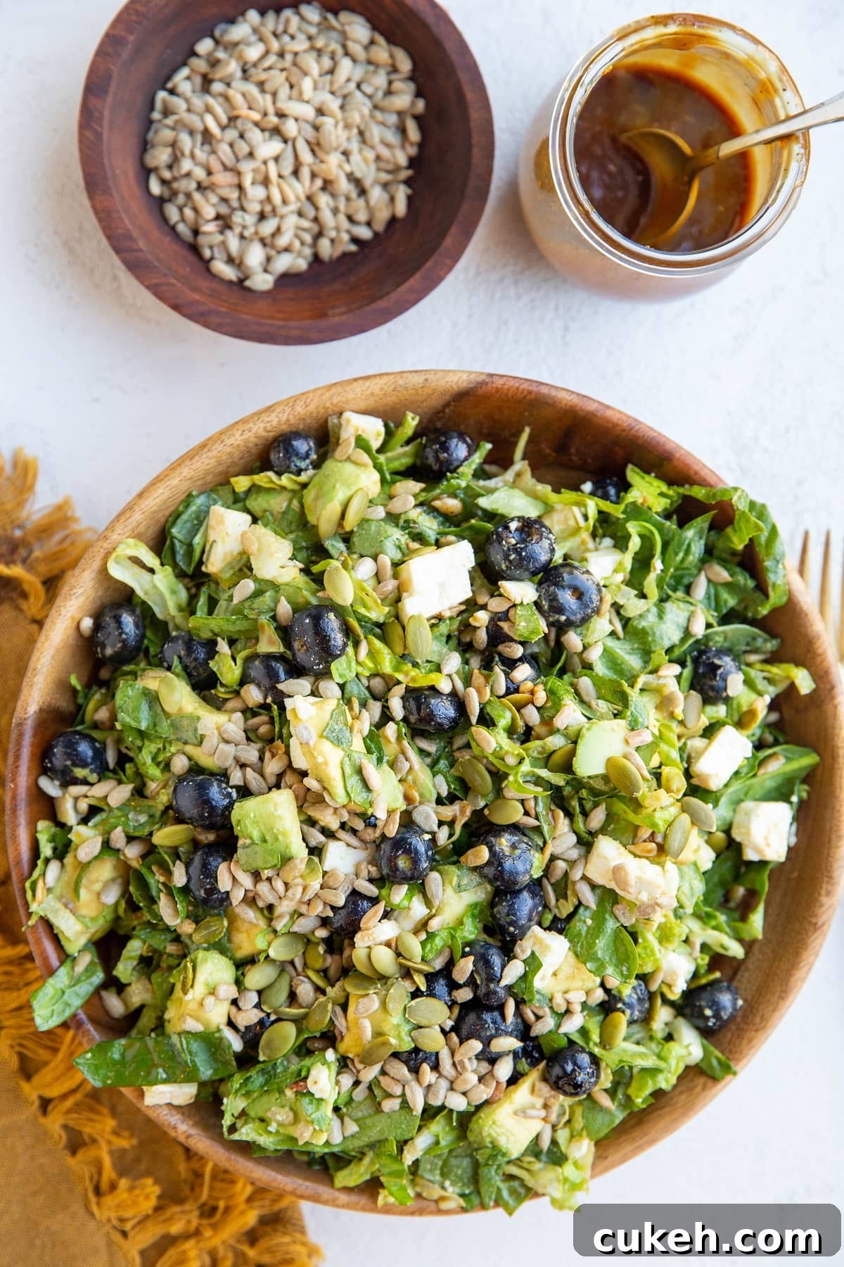 Bowl of green salad with blueberries, avocado, sunflower seeds, feta cheese, pumpkin seeds and balsamic vinaigrette mixed in.
