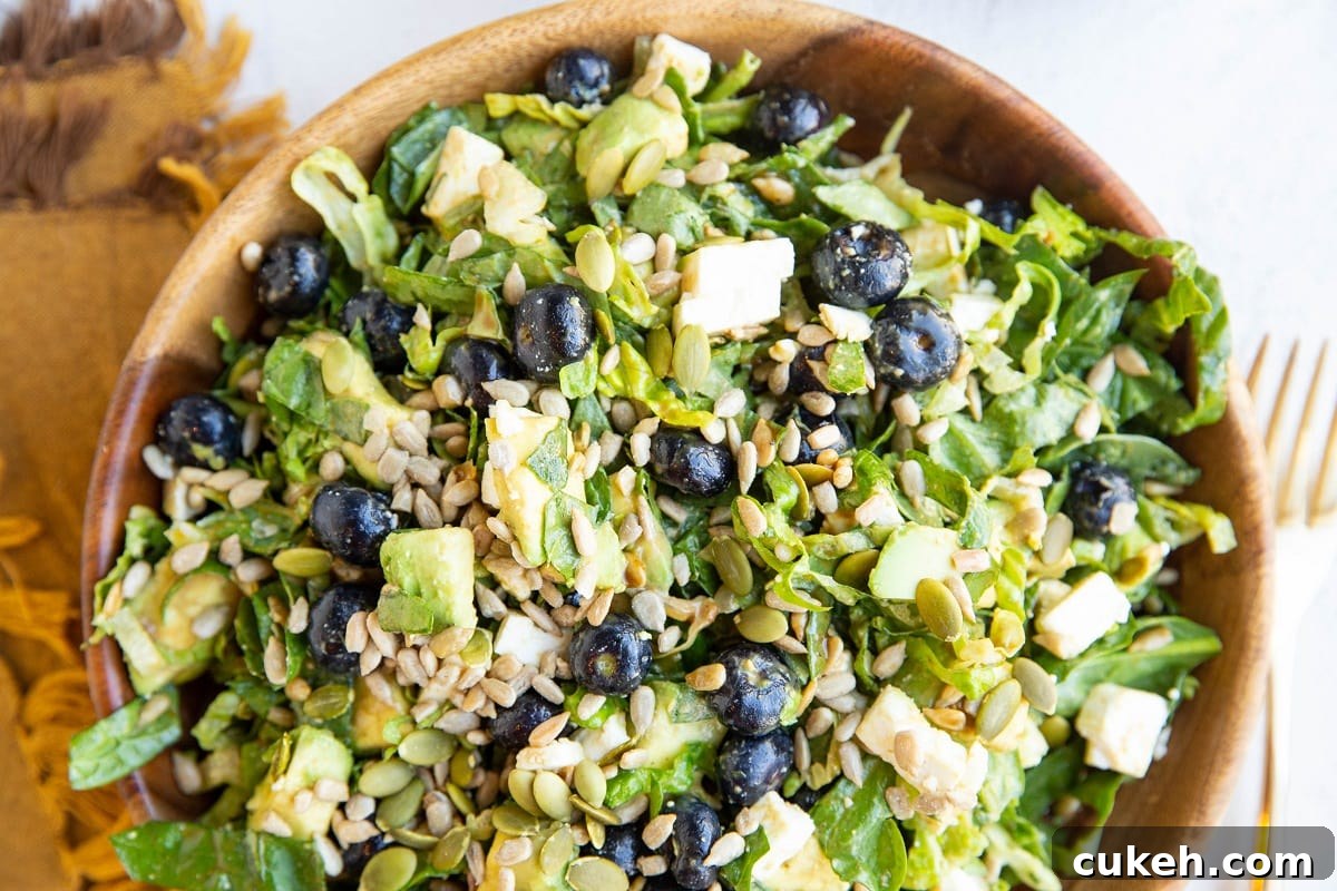 Big wooden bowl of chopped salad with a gold fork and napkin to the side.
