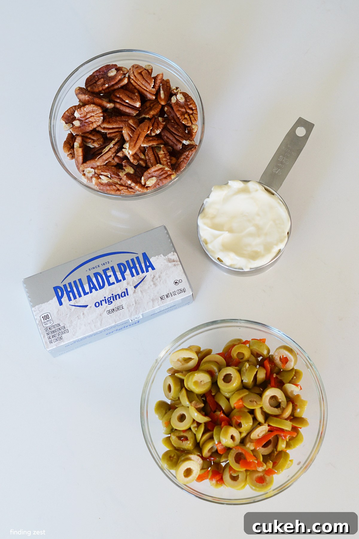 Ingredients for an olive dip including cream cheese, mayo, sliced green olives and chopped pecans.