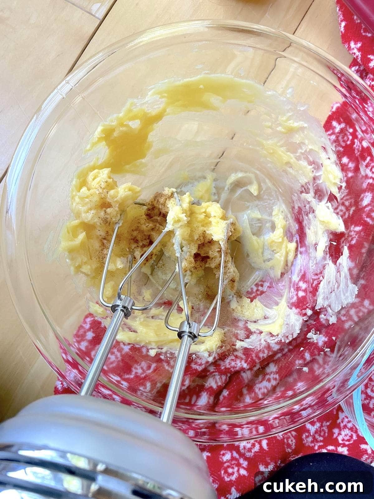 A small bowl of honey butter being whipped with an electric mixer, with cinnamon and vanilla extract being added to it.