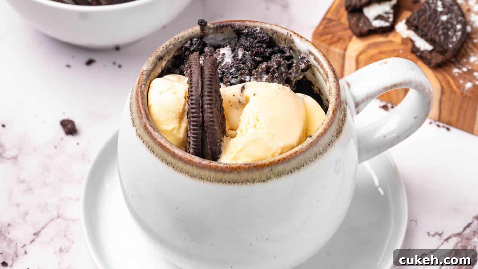 A white mug filled with vanilla ice cream, crushed chocolate sandwich cookies, and a whole cookie, placed on a saucer.
