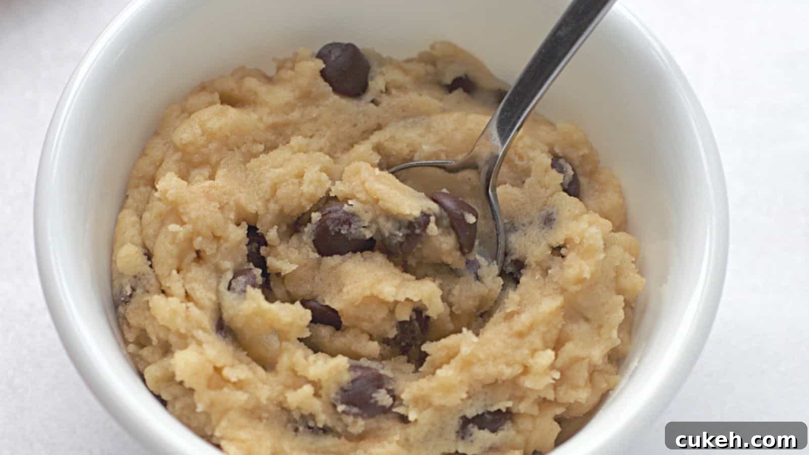 Edible chocolate chip cookie dough in white bowl with spoon.