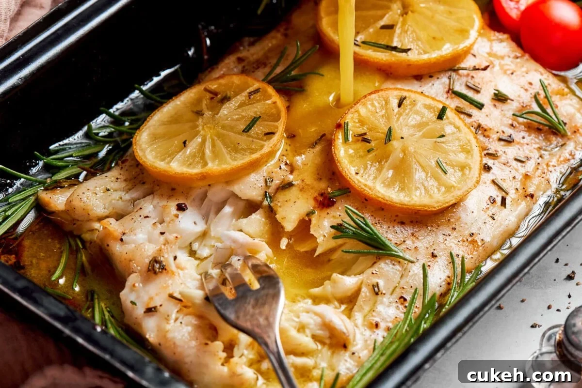 Champagne vinaigrette poured over baked halibut with lemon slices on a pan.